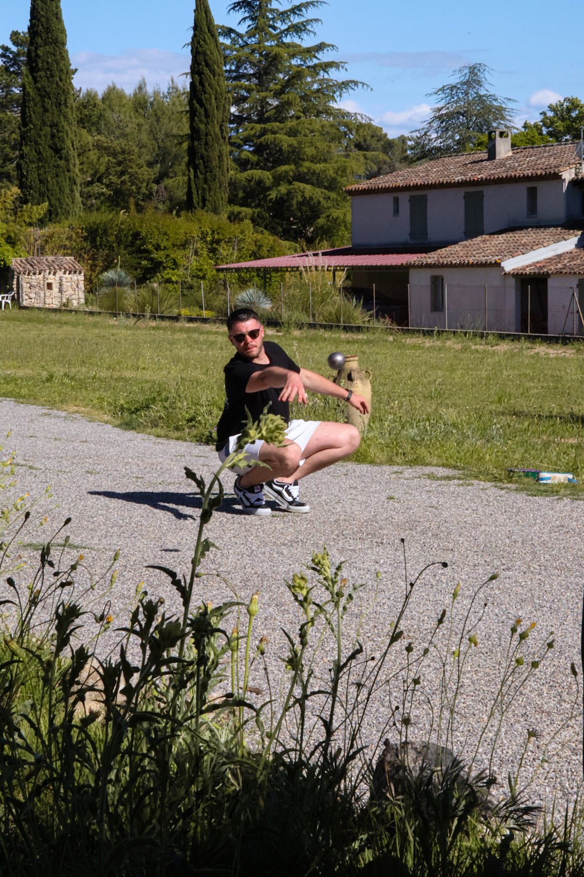 Joueur de pétanque en plein tir devant un mas provençal